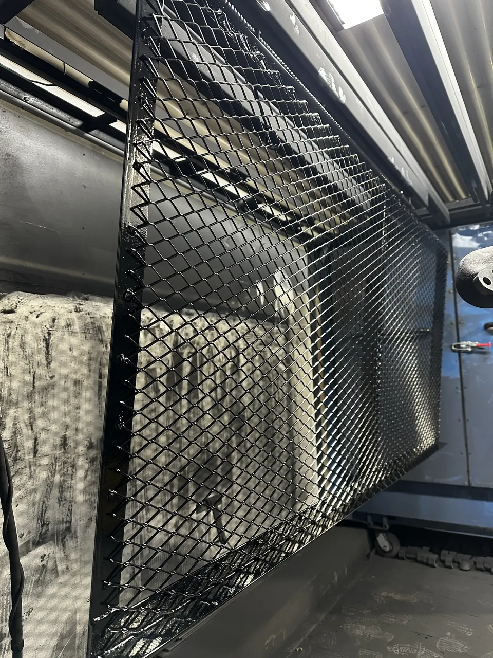 Black coated expanded-metal cover hanging from a rack in the finishing area